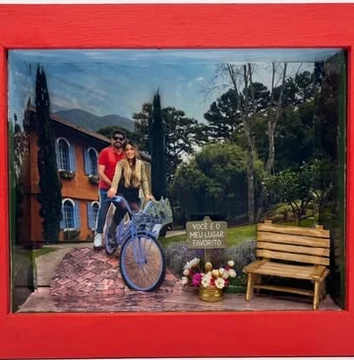 Caixa vermelha com a foto de um casal numa bicicleta, casa, jardim, banco e a placa “Você é o meu lugar favorito”