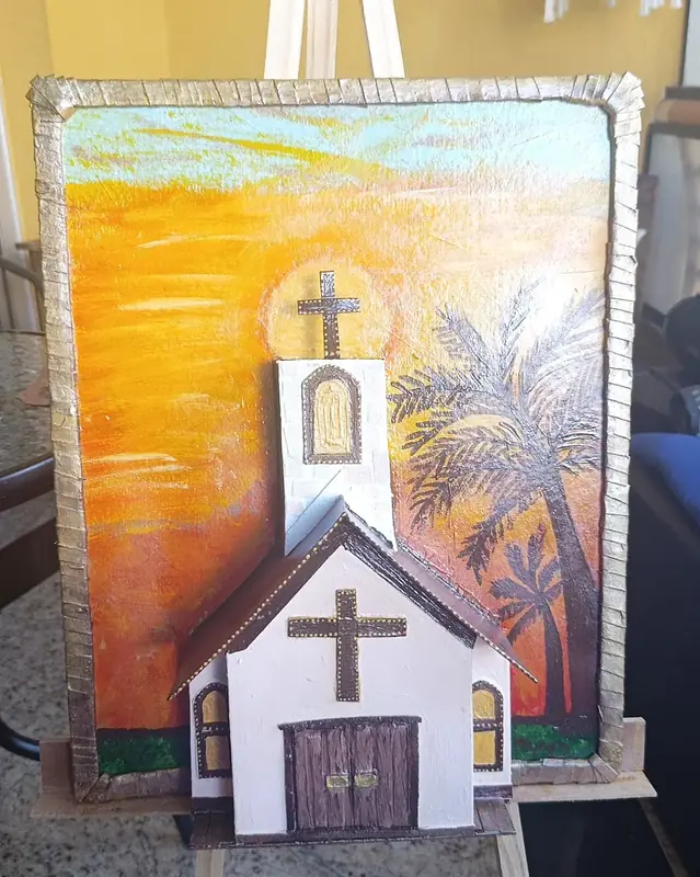 Igreja branca em relevo, com cruz e porta de madeira, diante de um pôr do sol alaranjado pintado à mão